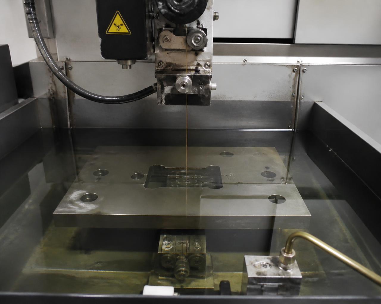 Wire EDM machine cutting a steel plate submerged in dielectric fluid in the work tank